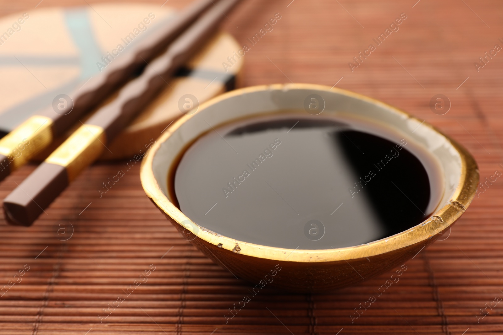 Photo of Bowl of soy sauce and chopsticks on bamboo mat, closeup