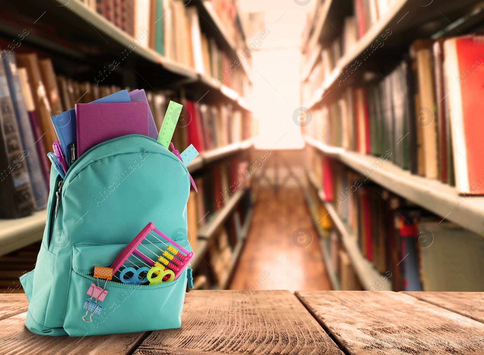 Image of Backpack with school stationery on wooden table in library, space for text