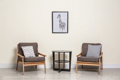 Room interior with modern armchairs and table near light wall