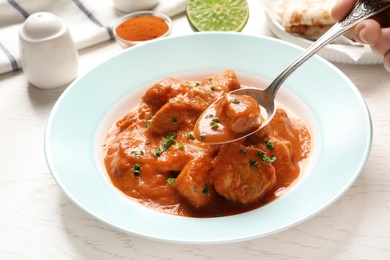 Photo of Woman eating tasty butter chicken at table, closeup. Traditional Murgh Makhani dish