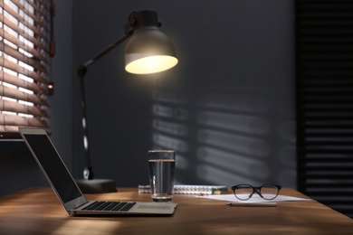 Photo of Modern laptop and lamp on table near window in office. Space for text