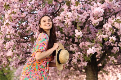 Beautiful woman with straw hat near blossoming tree on spring day