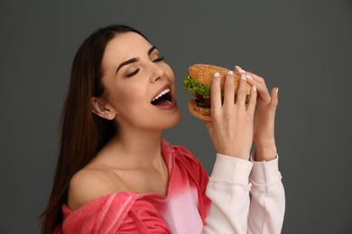 Photo of Young woman eating tasty burger on grey background