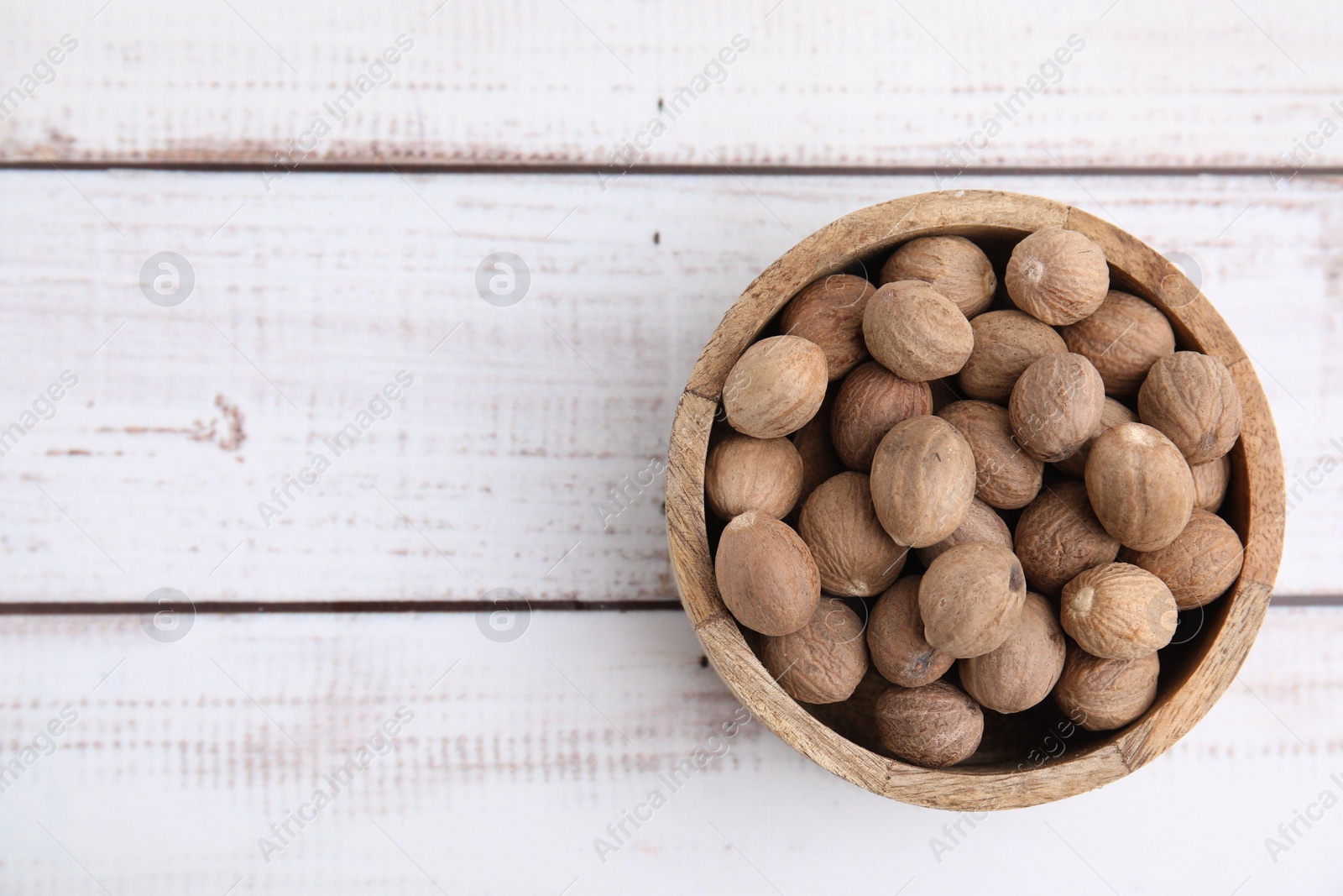 Photo of Whole nutmegs in bowl on light wooden table, top view. Space for text