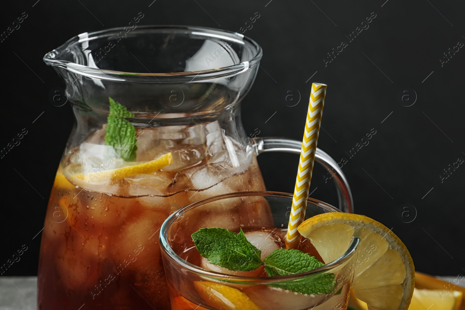 Photo of Jug and glass of delicious iced tea against black background, closeup