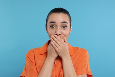 Photo of Embarrassed woman covering mouth on light blue background