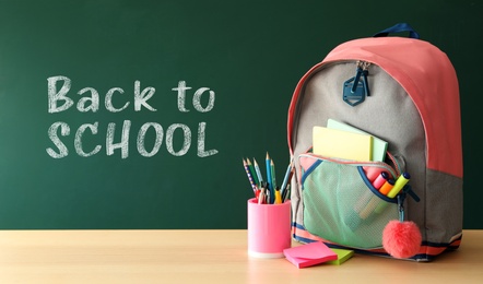 Image of Backpack and different stationery on wooden table near green chalkboard with text Back To School