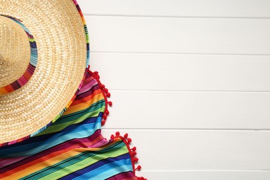 Photo of Mexican sombrero hat and colorful poncho on white wooden background, flat lay. Space for text