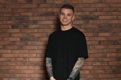 Photo of Smiling young man with tattoos near brick wall