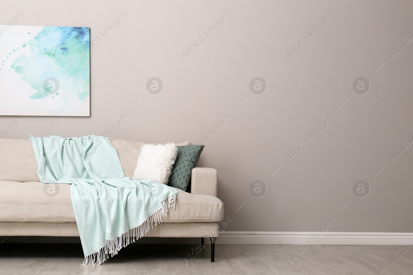 Photo of Modern comfortable sofa and picture near wall in room, space for text. Interior design