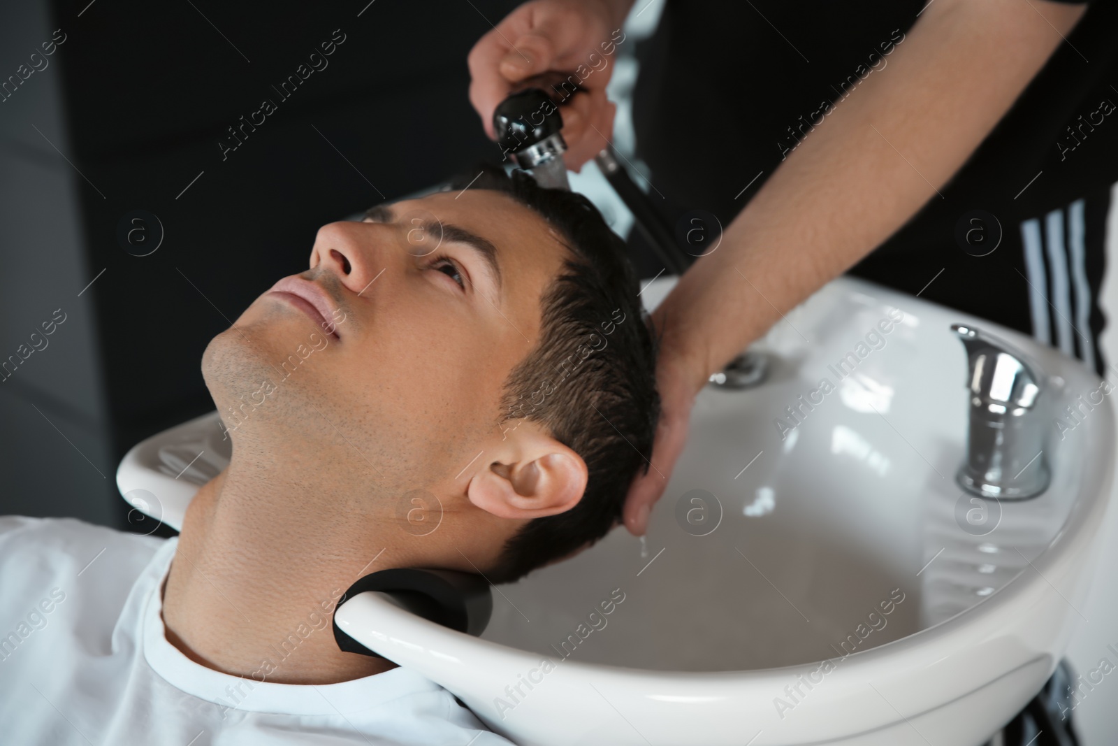 Photo of Professional barber washing client's hair at sink in salon, closeup