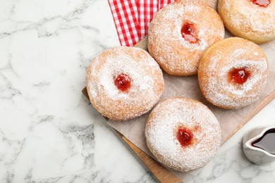 Photo of Delicious donuts with jam and powdered sugar on white marble table, flat lay. Space for text