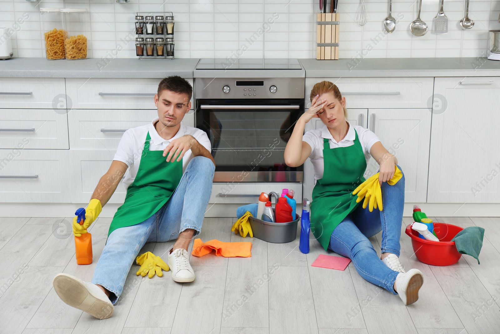 Photo of Exhausted janitors sitting on floor in kitchen. Cleaning service