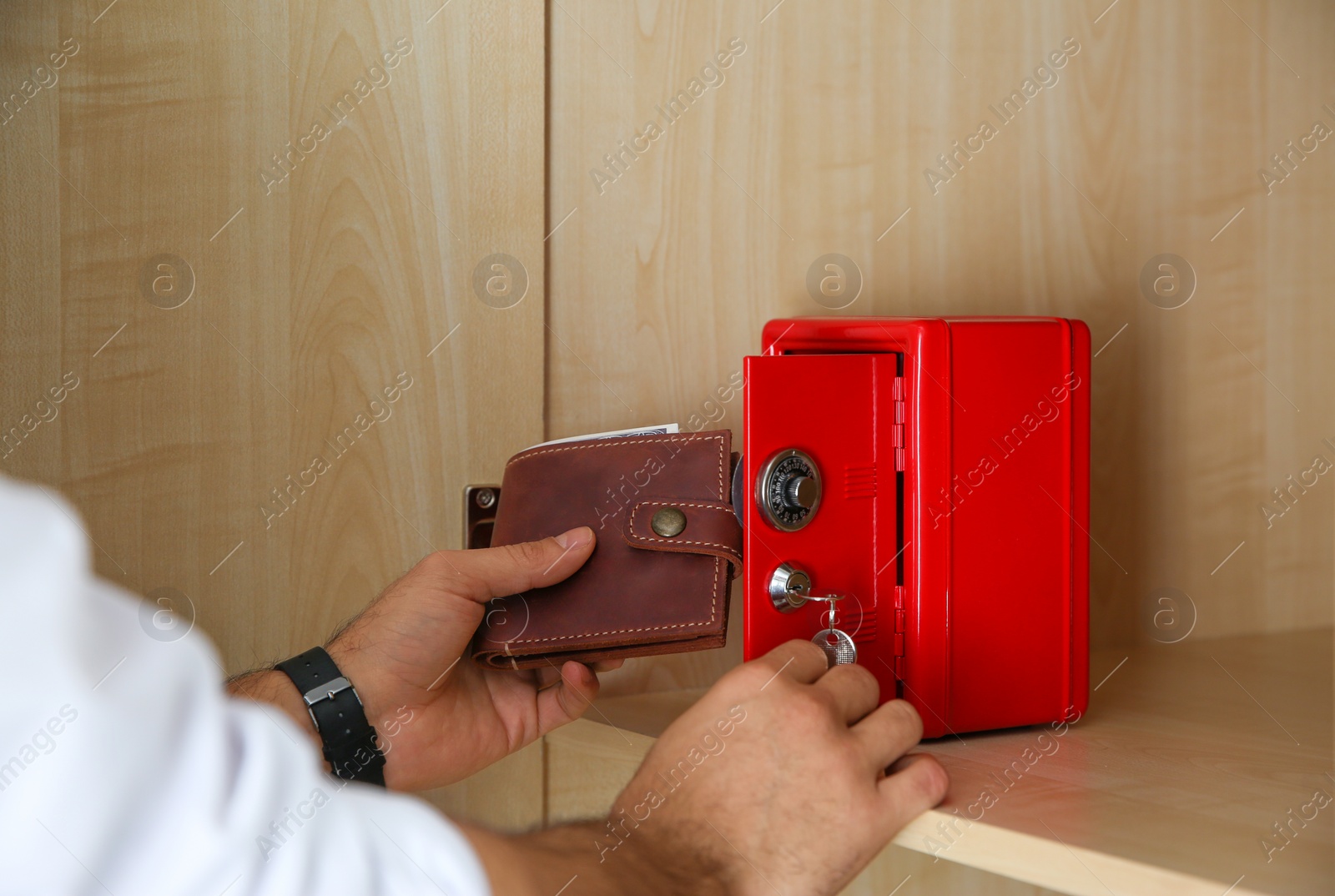 Photo of Man putting wallet into small red steel safe, closeup