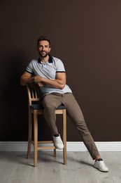 Photo of Handsome man sitting on stool near brown wall