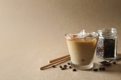 Photo of Refreshing iced coffee with milk in glass, straws and beans on beige background. Space for text