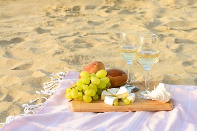 Photo of Glasses with white wine and snacks for beach picnic on sand outdoors