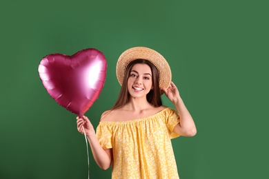 Portrait of young woman with heart shaped balloon on color background