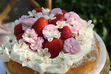 Photo of Delicious homemade cake decorated with fresh strawberries and spring flowers on table in garden, closeup