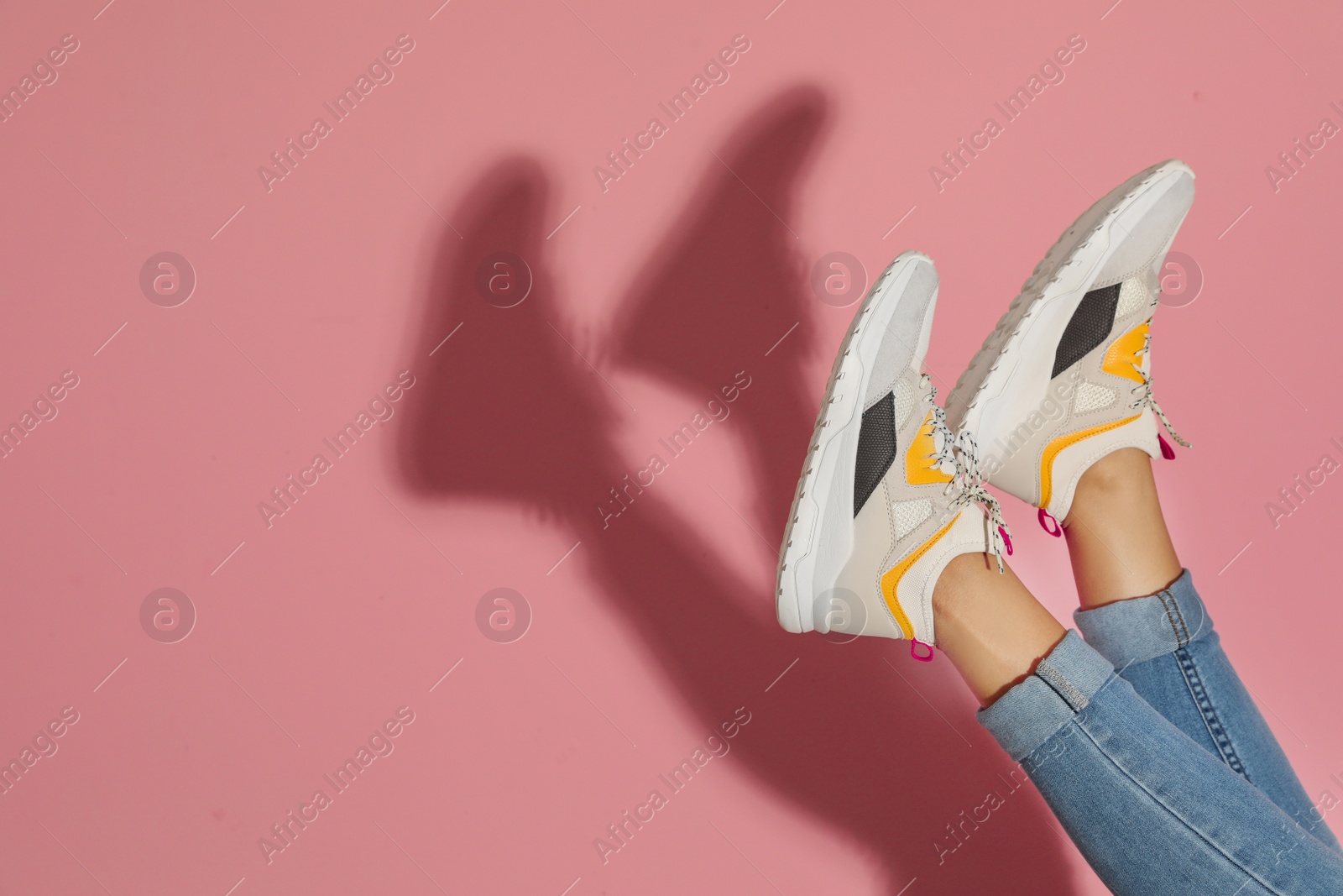 Photo of Woman in stylish sneakers near color wall, closeup. Space for text