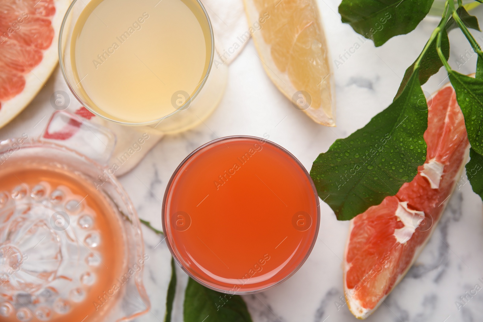 Photo of Glasses of different pomelo juices and fruits on white marble table, flat lay