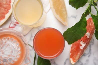 Glasses of different pomelo juices and fruits on white marble table, flat lay