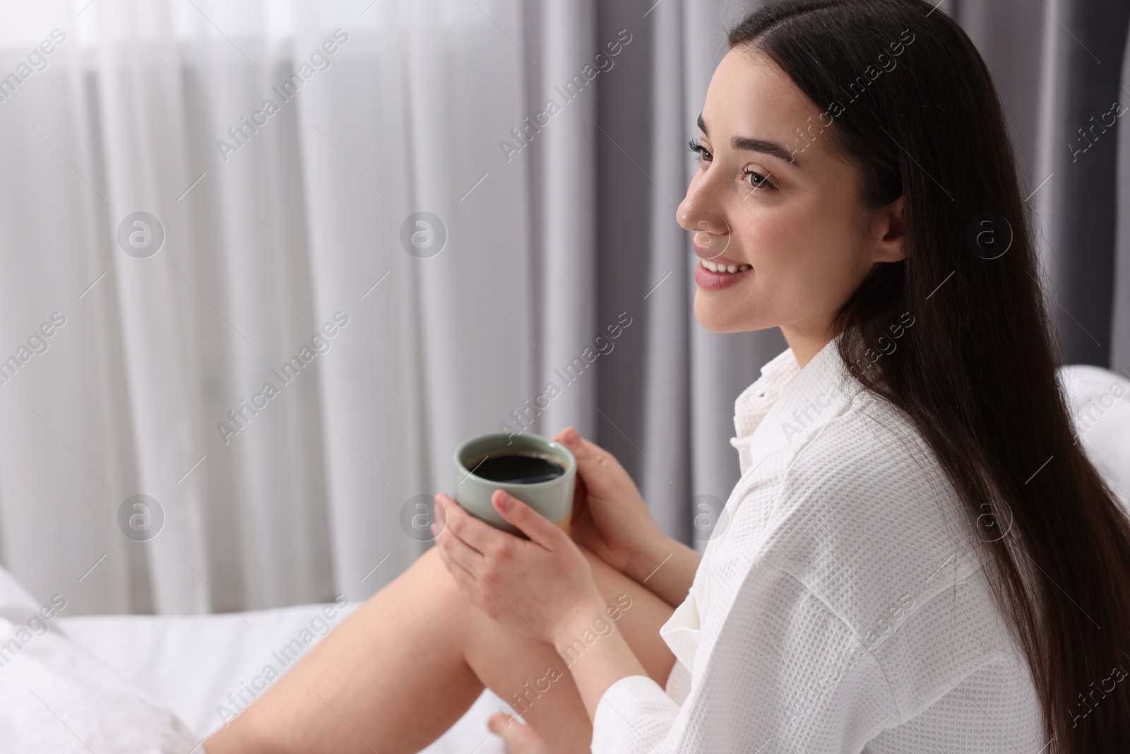 Photo of Happy woman with cup of drink on bed at home, space for text. Lazy morning