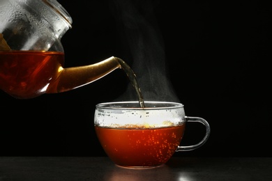 Photo of Pouring delicious hot tea into glass cup on table against dark background