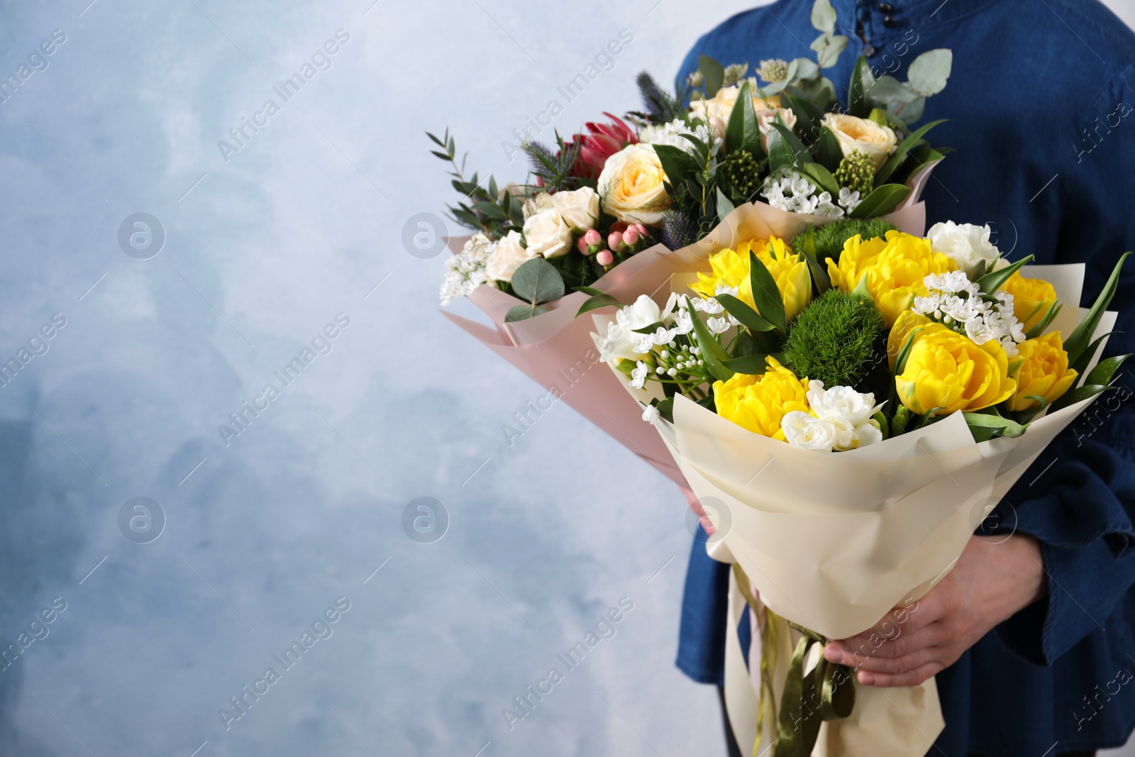 Photo of Woman with bouquets of beautiful flowers on light blue background, closeup. Space for text