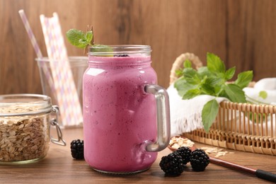 Photo of Delicious blackberry smoothie in mason jar, oatmeal and berries on wooden table