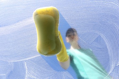 Woman cleaning glass with sponge on sunny day