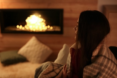 Photo of Young woman resting near decorative fireplace at home. Winter season