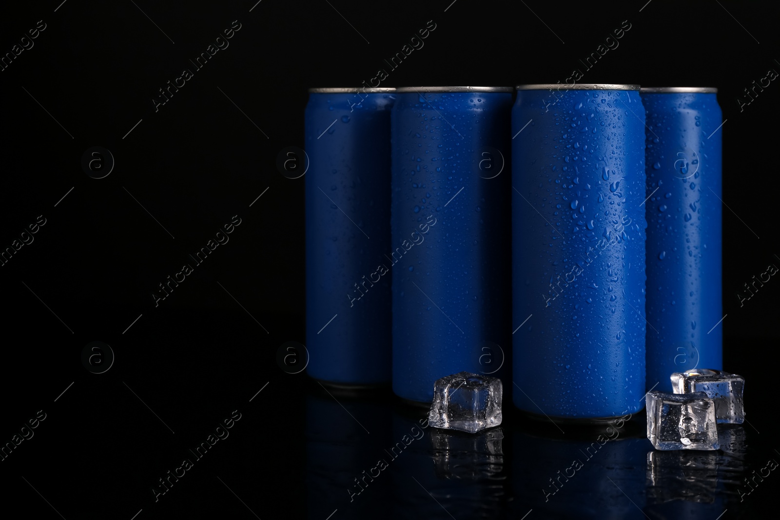 Photo of Energy drinks in wet cans and ice cubes on black background, space for text