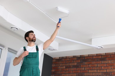 Photo of Handyman painting ceiling with roller in room