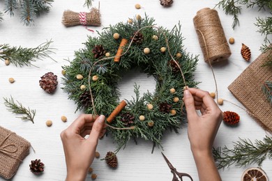 Photo of Florist making beautiful Christmas wreath at white wooden table, top view