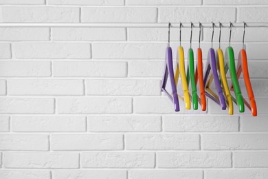 Photo of Colorful clothes hangers on rail near white brick wall. Space for text