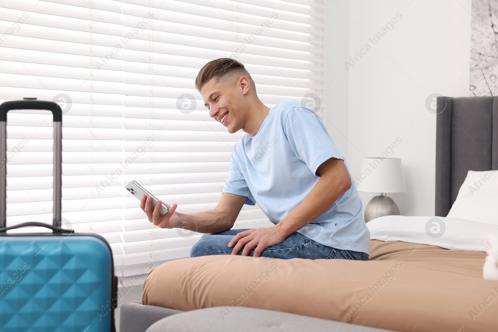 Photo of Smiling guest with smartphone on bed in stylish hotel room