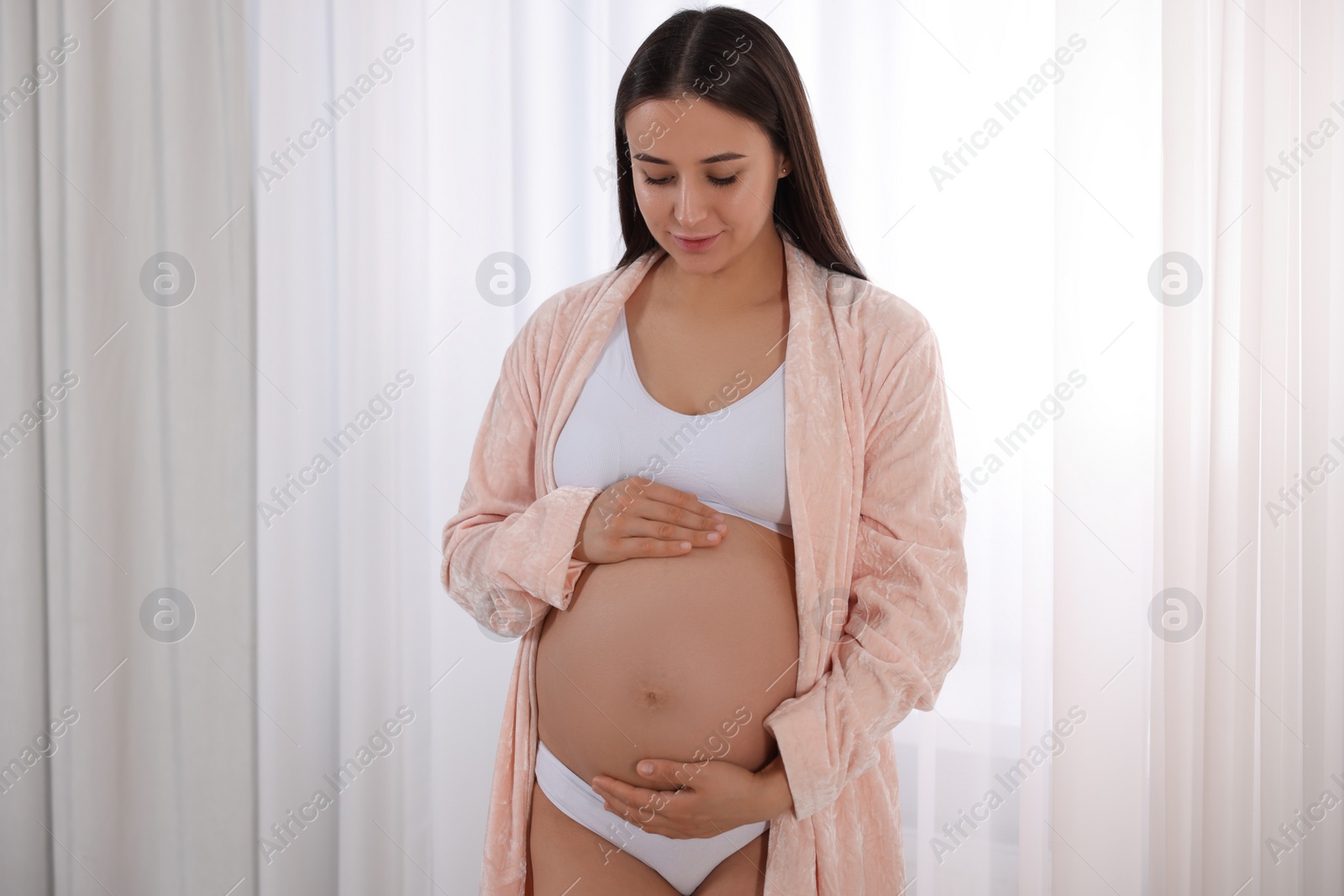 Photo of Beautiful pregnant woman in stylish comfortable underwear and robe indoors