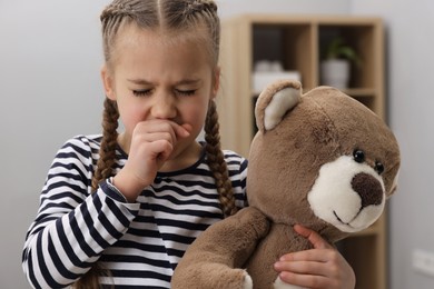 Sick girl with teddy bear coughing at home