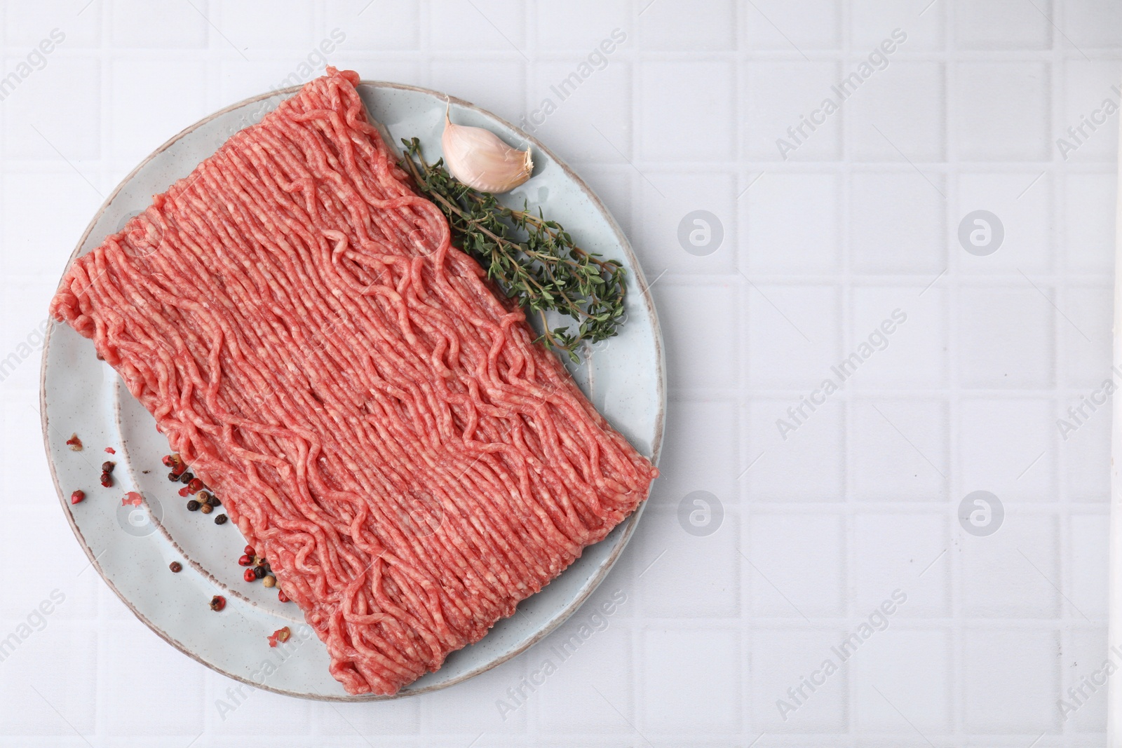 Photo of Fresh raw ground meat, peppercorns, garlic and thyme on white tiled table, top view. Space for text