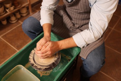 Photo of Man crafting with clay on potter's wheel indoors, closeup
