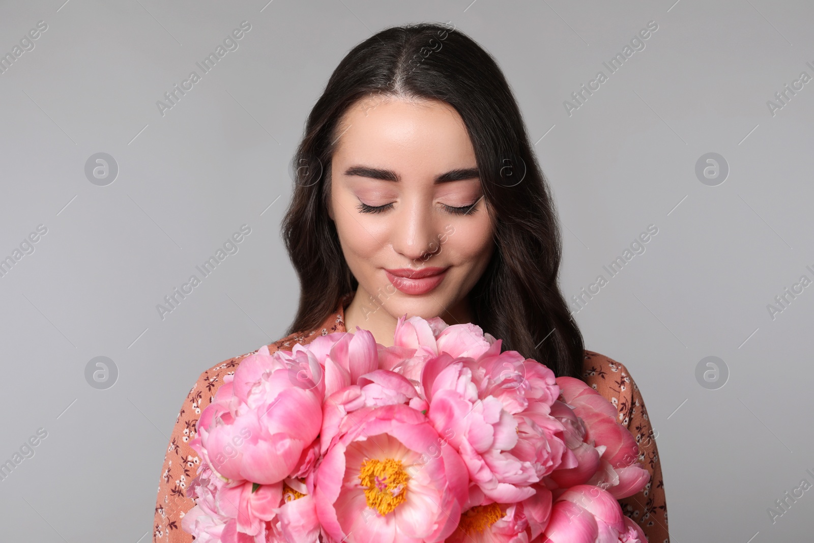 Photo of Beautiful young woman with bouquet of peonies on light grey background