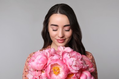 Beautiful young woman with bouquet of peonies on light grey background