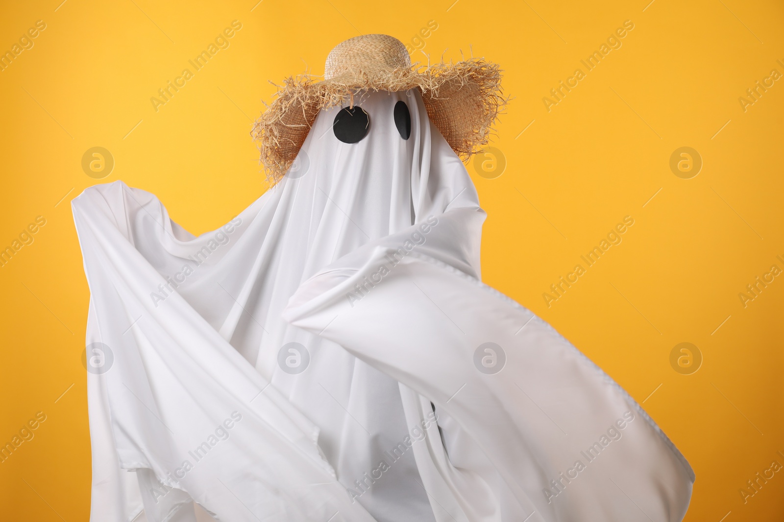 Photo of Person in ghost costume and straw hat on yellow background