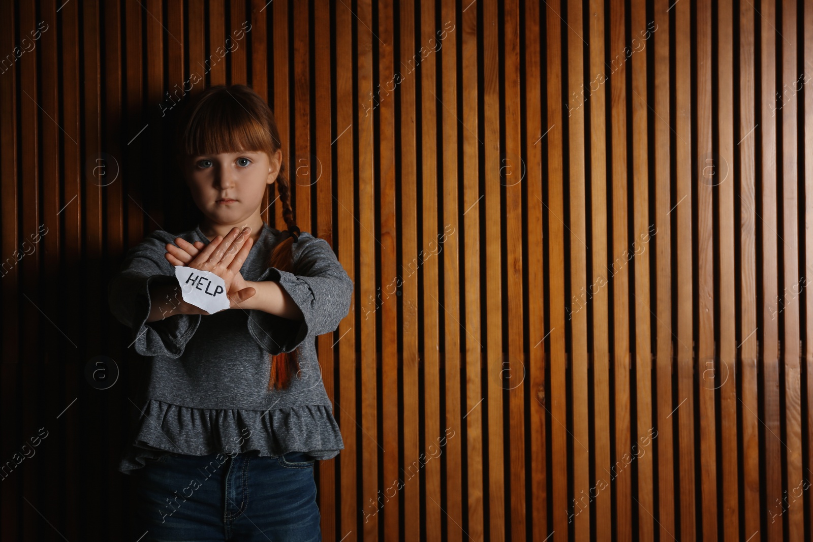 Photo of Sad little girl with sign HELP on wooden background, space for text. Child in danger