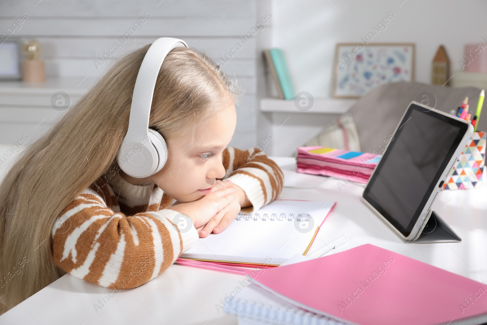 Photo of Cute little girl with modern tablet studying online at home. E-learning