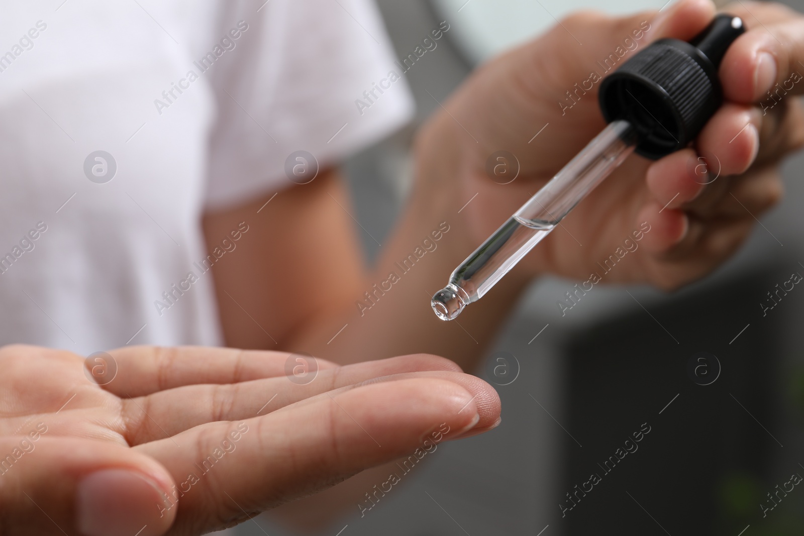 Photo of Woman applying cosmetic serum onto her finger on blurred background, closeup