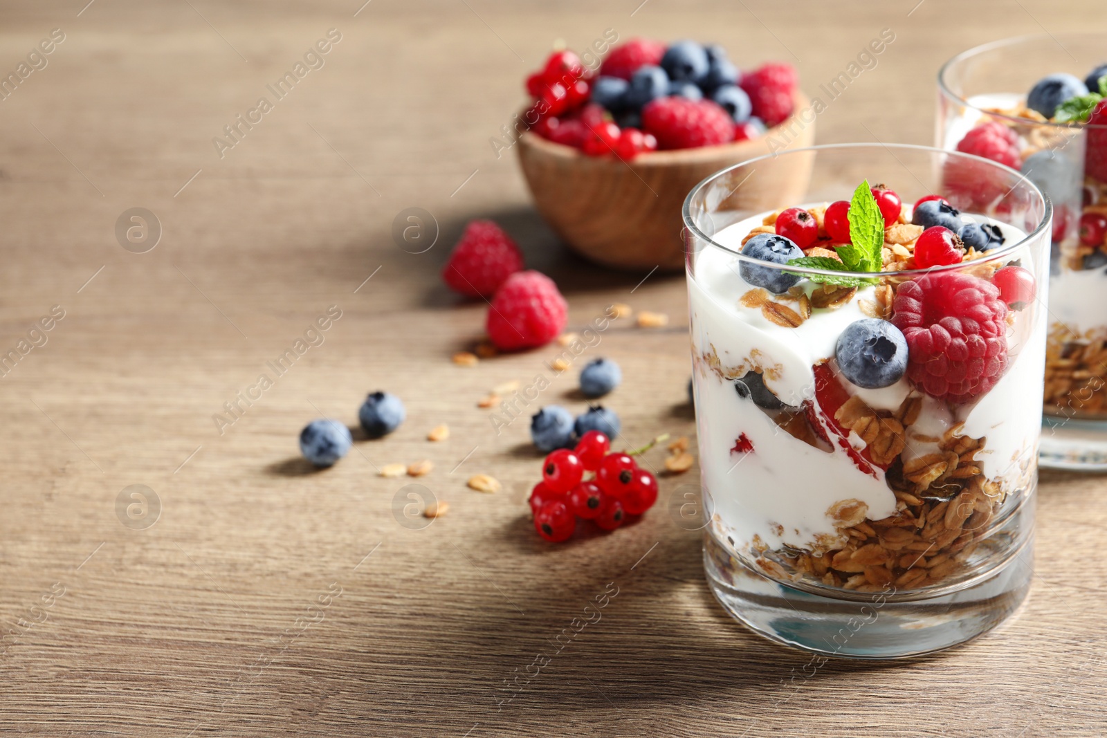 Image of Tasty dessert with yogurt, berries and granola on wooden table. Space for text 