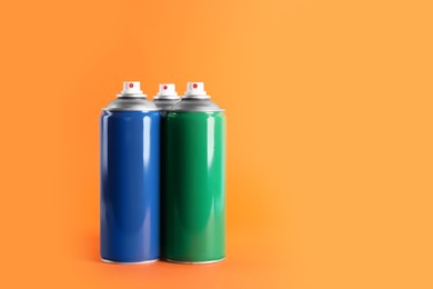 Colorful cans of spray paints on orange background. Space for text