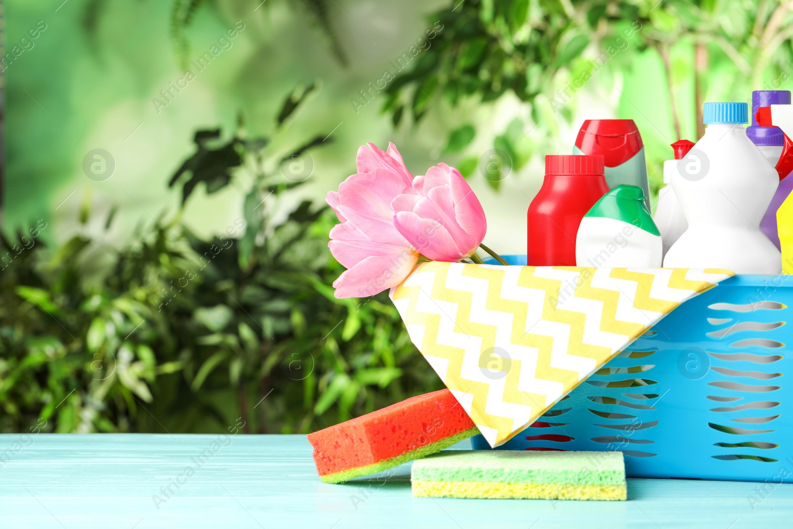 Photo of Plastic basket with spring flowers and cleaning supplies on light blue wooden table. Space for text